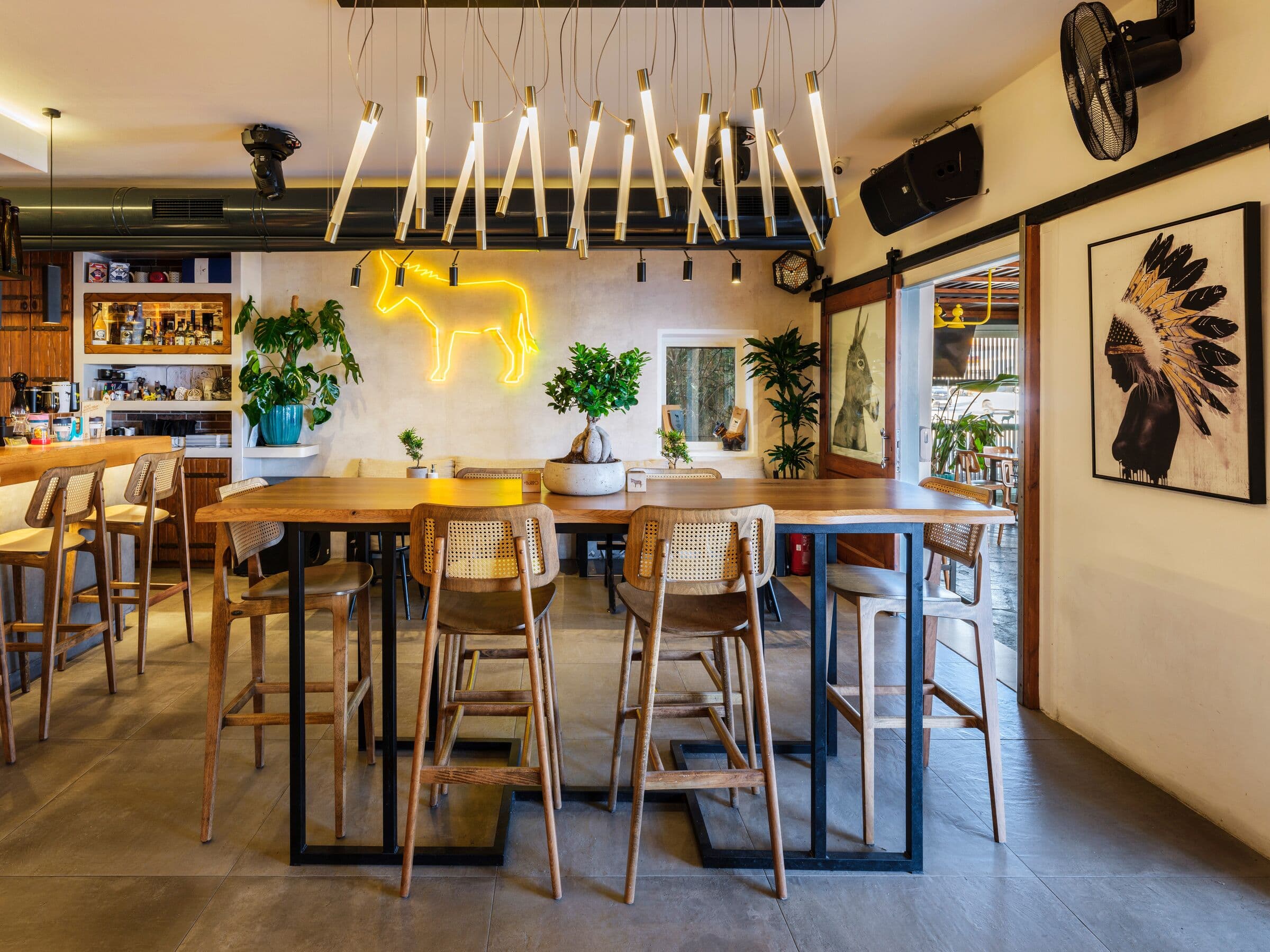 The bar room: high wooden tables, rattan stools, the yellow neon donkey and a long pendant light