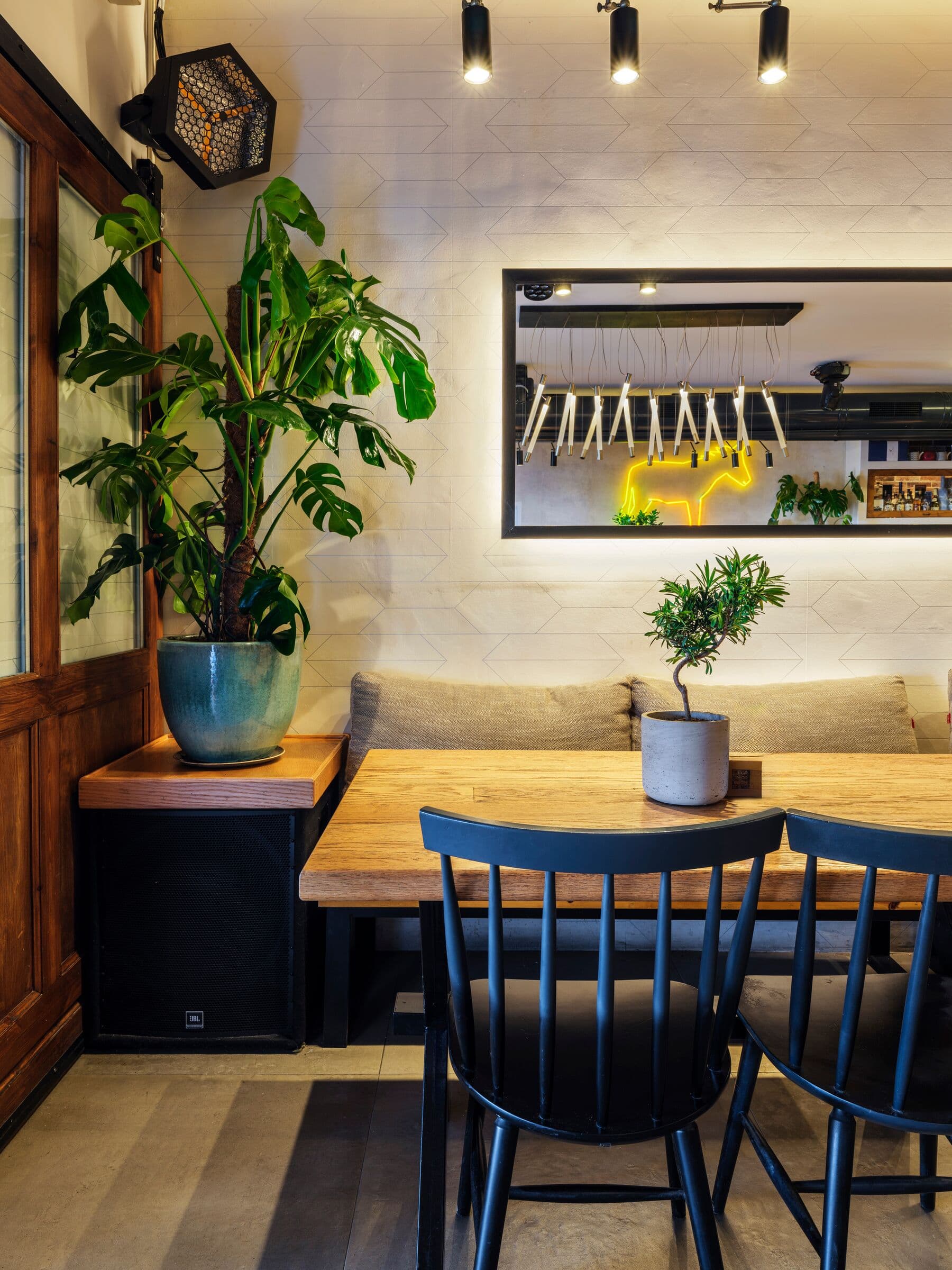 A corner table by the window with black chairs, a tall monstera and the neon donkey in the mirror